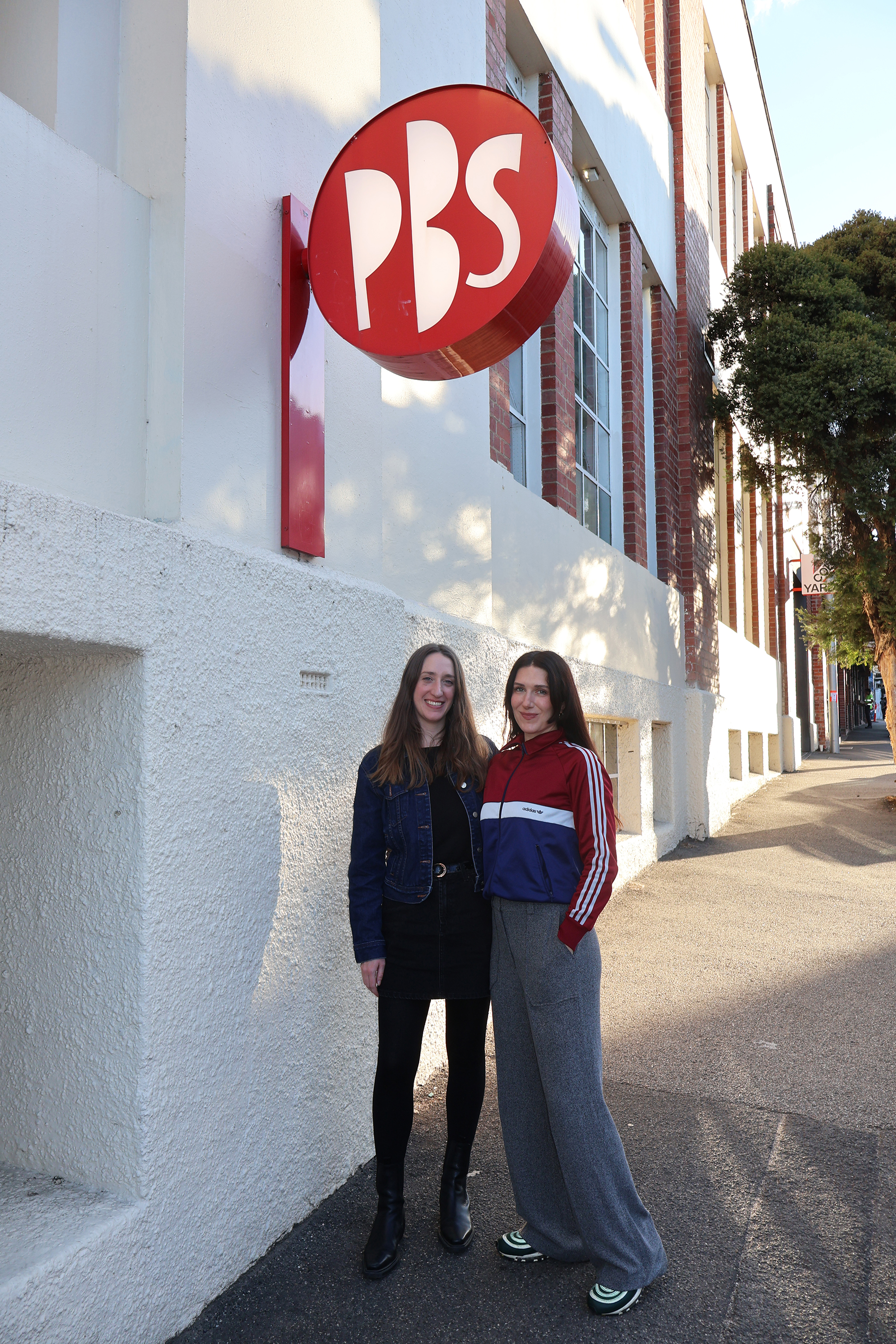 PBS alumni Amy Chapman and PBS announcer Elle Young stand under the PBS sign on Johnston Street