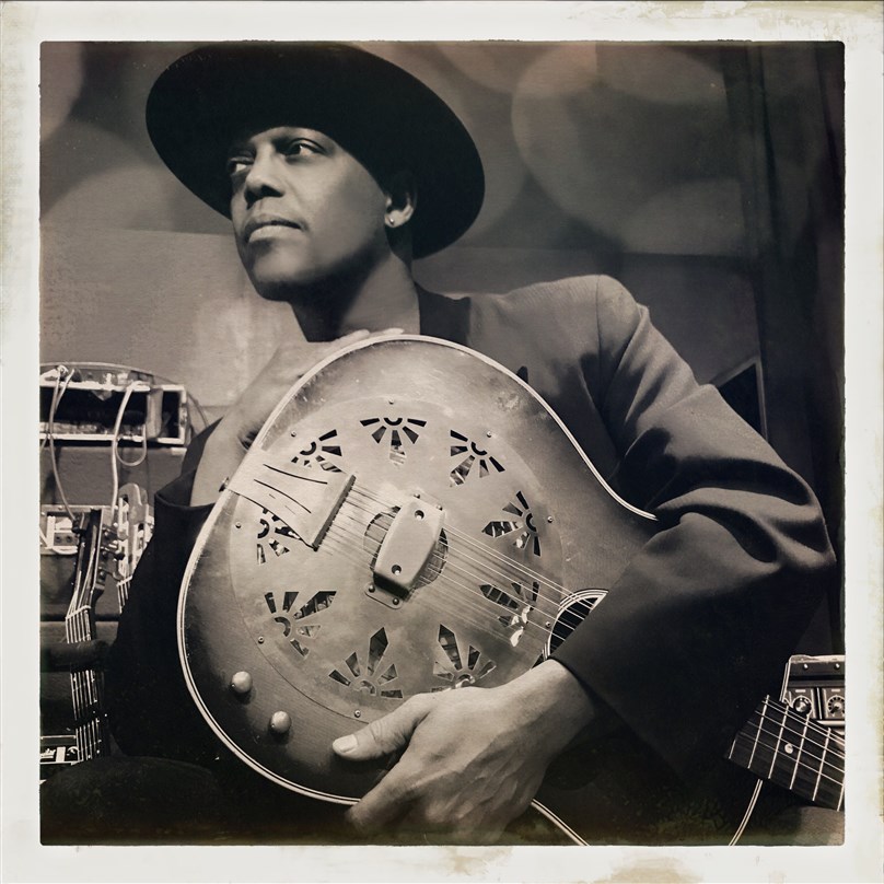 A sepia photo of Eric Bibb holding a guitar