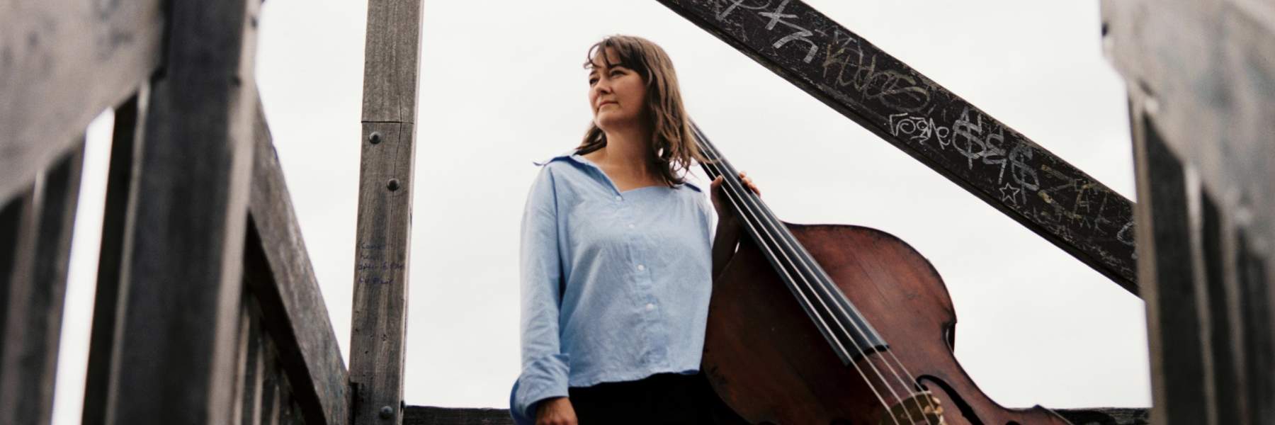 Tamara Murphy standing at the top of a staircase outside with a double bass.