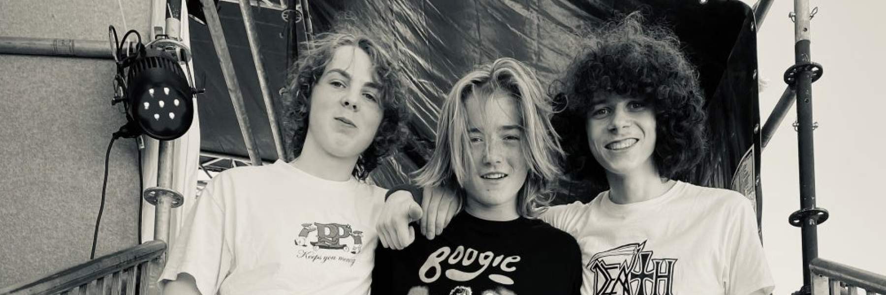 Three members of Cheeky Geezers smiling and standing on steps leading up to a stage