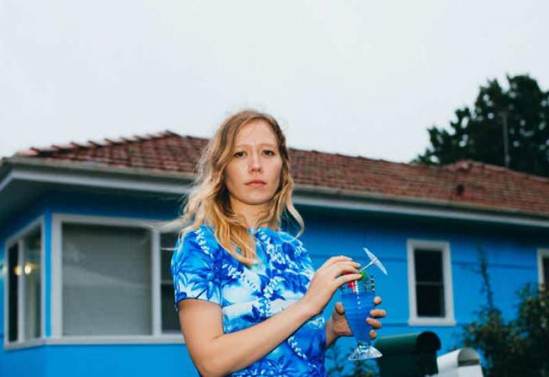 Julia Jacklin wears a blue shirt in front of a blue house